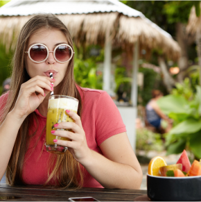 A woman sitting at an outdoor table drinking juice.